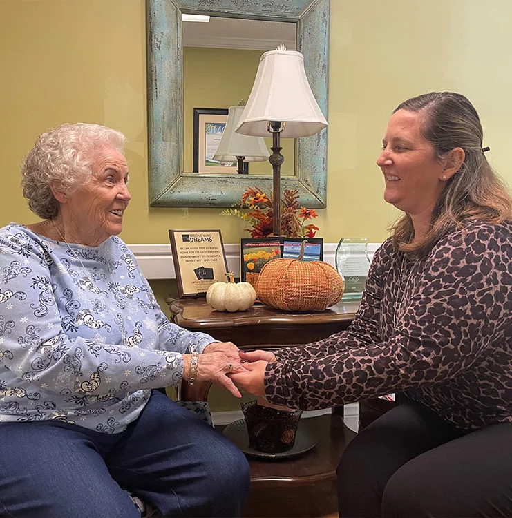 A woman and an older woman sitting in a chair, engaged in conversation.