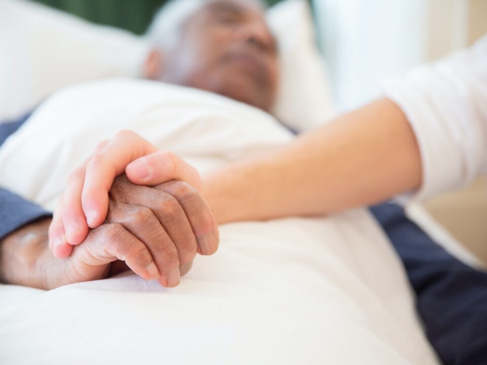 Nurse holding elderly man's hands in bed