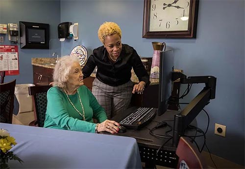 A man and woman in a gym room, the man is assisting the woman in a wheelchair with exercises.